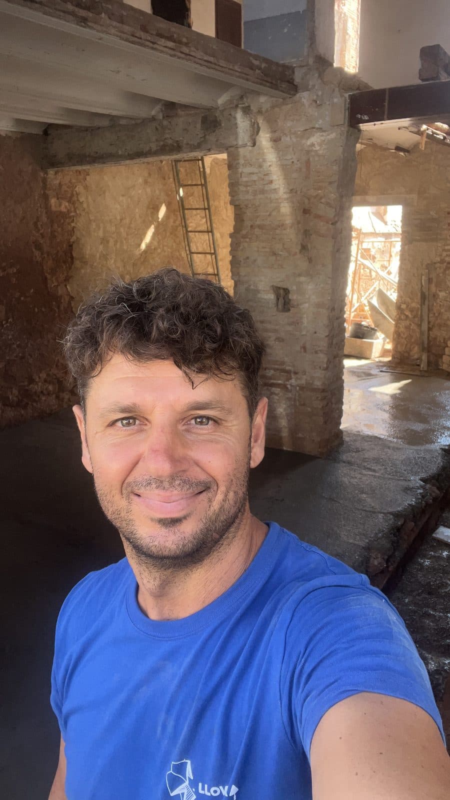 Emilio José Llovera Asensi, sonriente y con la camiseta de la empresa, dentro de una casa en obra con los muros de piedra y ladrillo a la vista